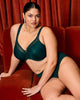 Curvy woman wearing Smooth Full cup bra in deep emerald green made for plus size boobs and bodies on a velvet couch lifestyle looking sexy