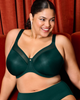 Curvy woman smiling wearing Smooth Full cup bra in deep emerald green made for plus size boobs and bodies on a velvet couch lifestyle